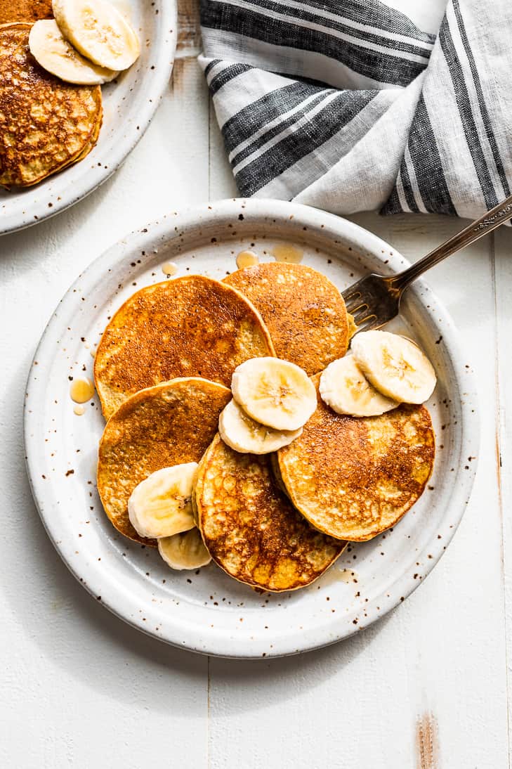 Looking down on a plate of banana pancakes with banana slices on top.