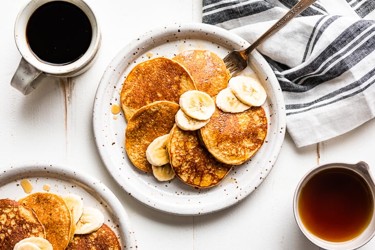 Two plates of banana pancakes and two cups of coffee.