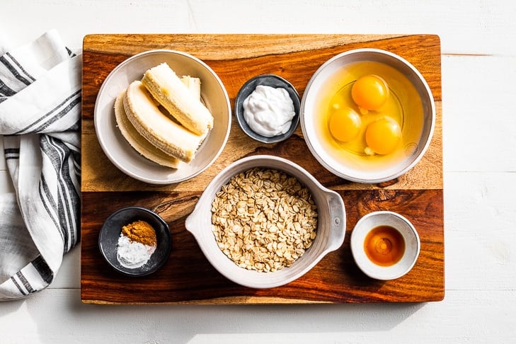 All the ingredients for Healthy Banana Pancakes prepped and on a wooden cutting board.