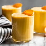 Three glasses of creamsicle smoothie sitting on a marble backdrop with a stripped linen.