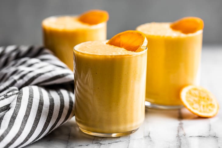 Three glasses of creamsicle smoothie sitting on a marble backdrop with a stripped linen.