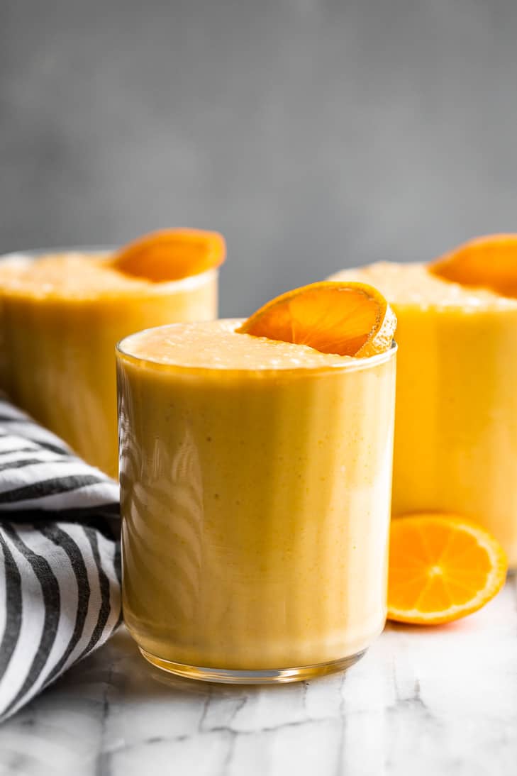 Three glasses of Orange Creamsicle Smoothie with a striped linen on the side.