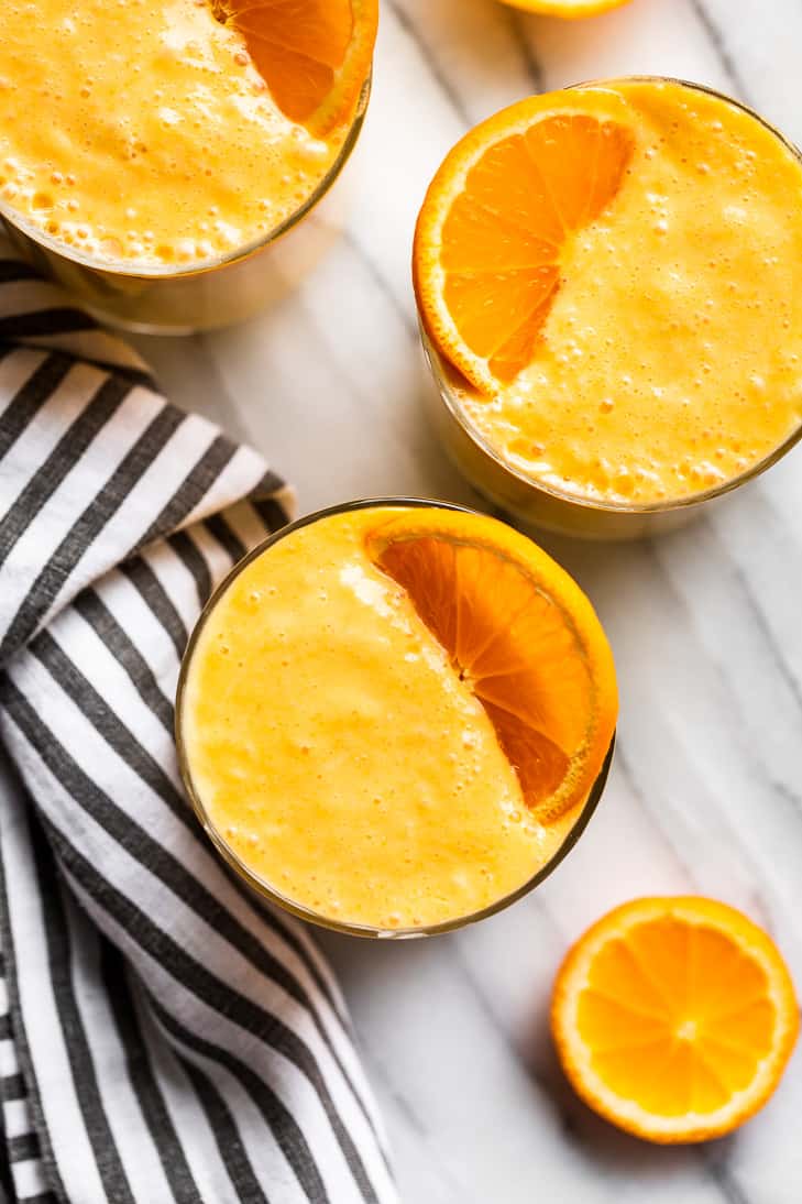 Looking straight down on three glasses of Orange Creamsicle Smoothie with orange slices on top.