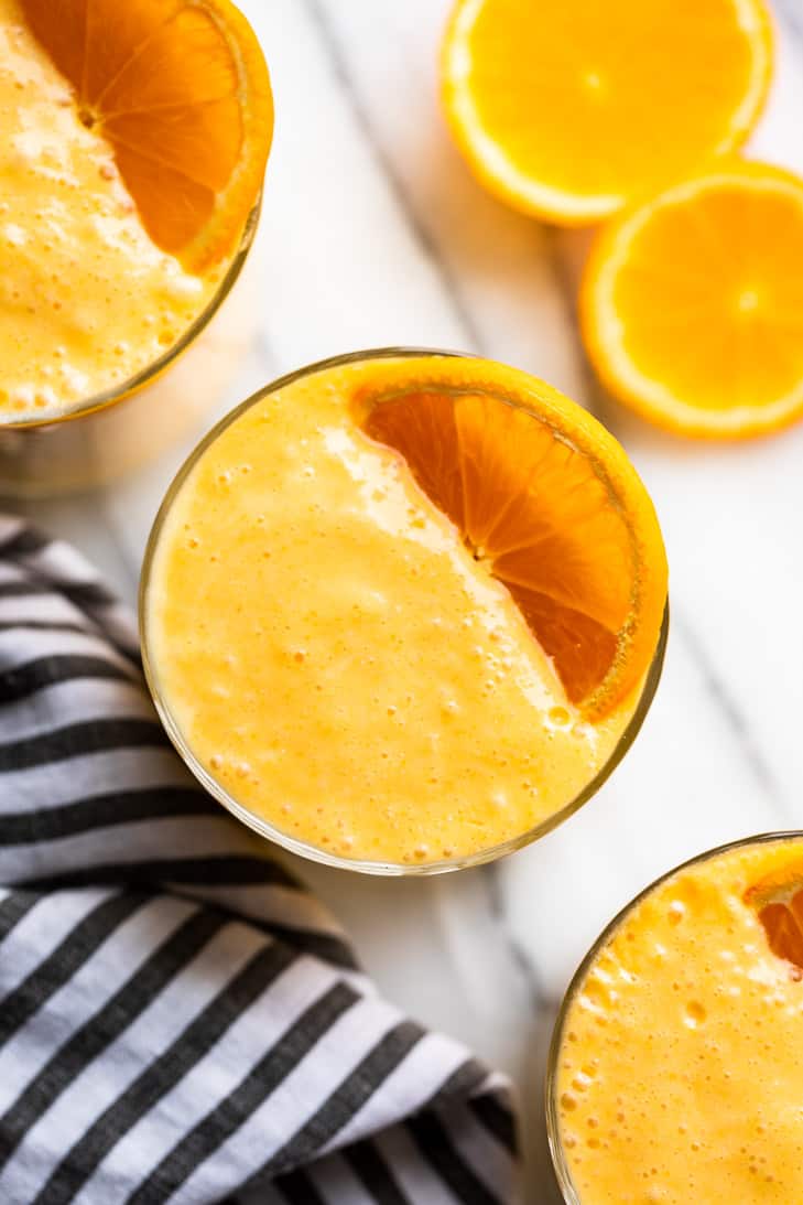 Three glasses of creamsicle smoothie in a row with orange slices on the side.