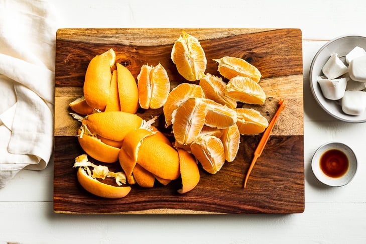 Peeled oranges and the smoothie ingredients prepped and sitting on a wooden cutting board.