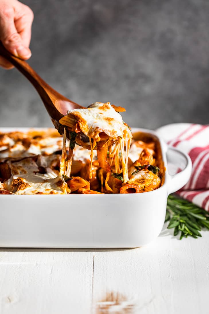 A spoonful of Simple Veggie Pasta Bake being lifted out of the baking dish with strings of cheese coming down.