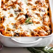 Finished pasta bake in a white baking dish with a wooden spoon and a sprig of rosemary.