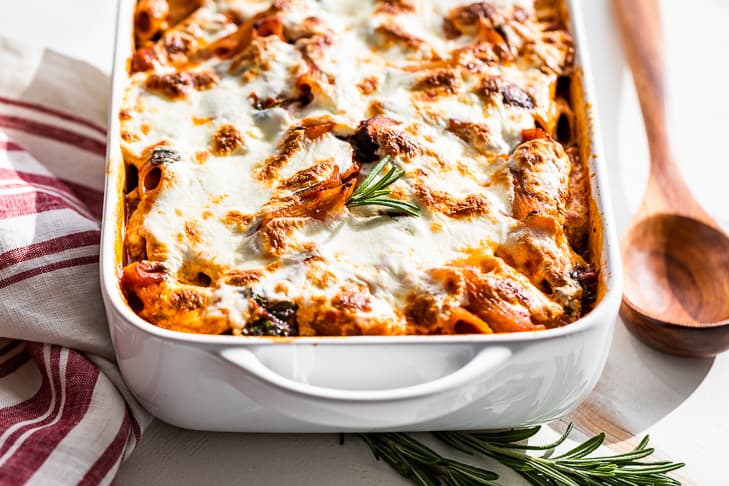 Finished pasta bake in a white baking dish with a wooden spoon and a sprig of rosemary.