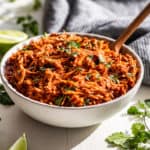 A white bowl filled with Slow Cooker Chipotle Chicken with cilantro and lime wedges around it.