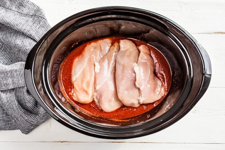 Adding the chicken breasts to the sauce in the slow cooker.