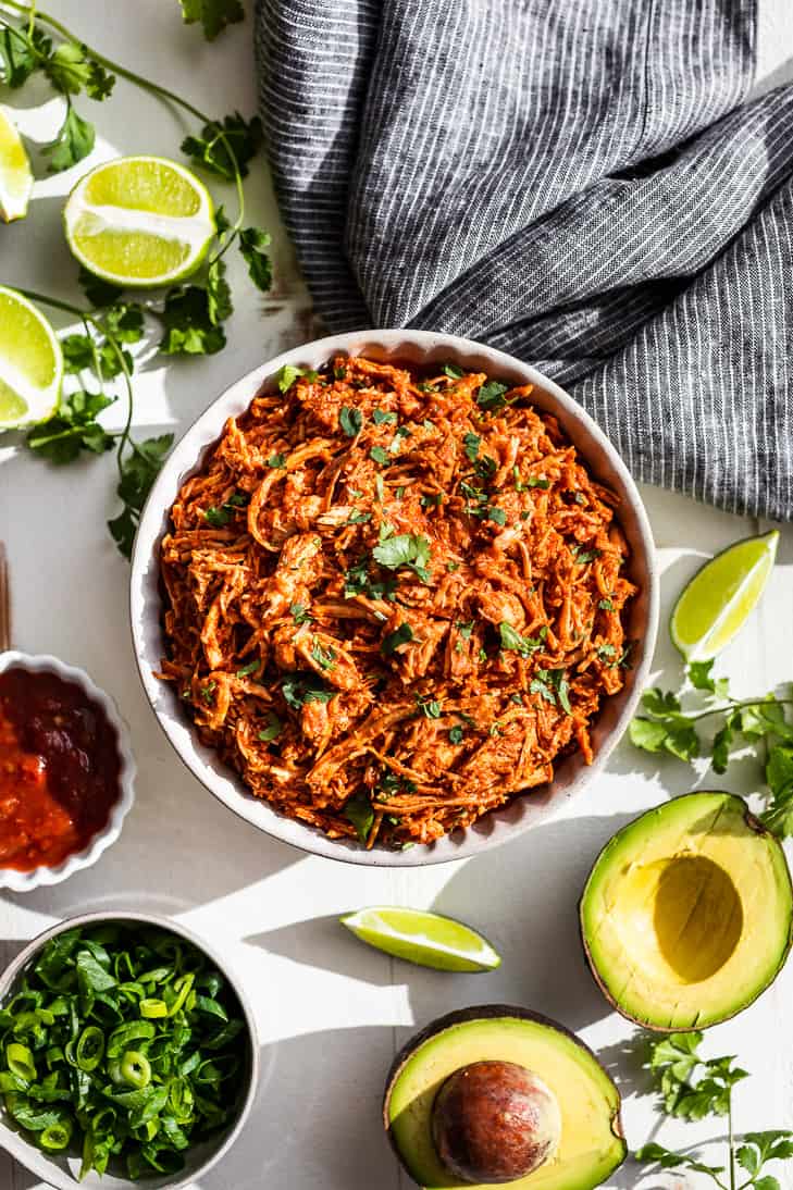 A white bowl filled with Slow Cooker Chipotle Chicken with toppings around it.