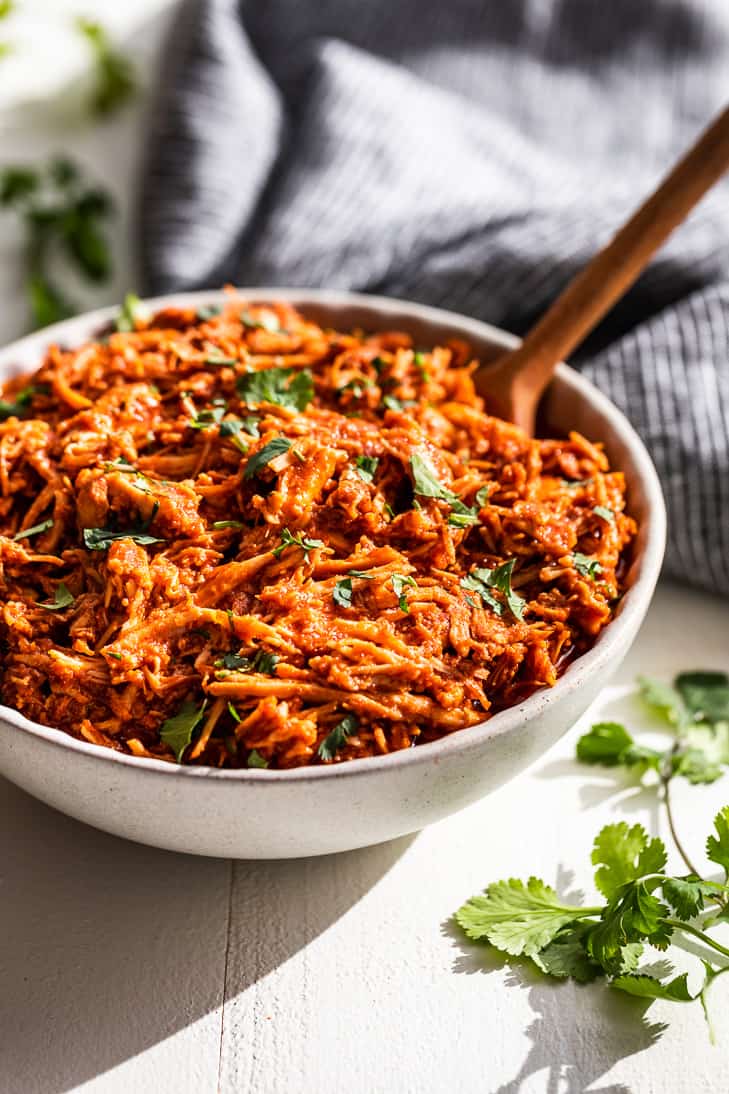 A white bowl filled with Slow Cooker Chipotle Chicken with cilantro sprigs around it.