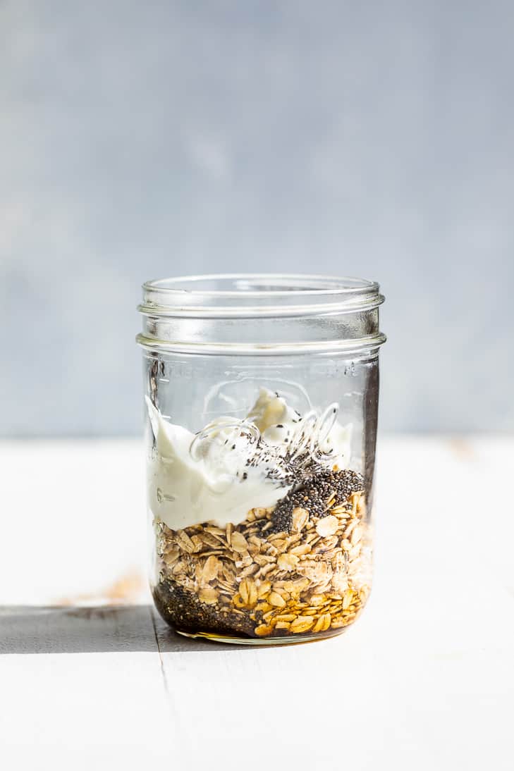 The oats, maple syrup, chia seeds, and yogurt added to a 2 cup mason jar on a white background.