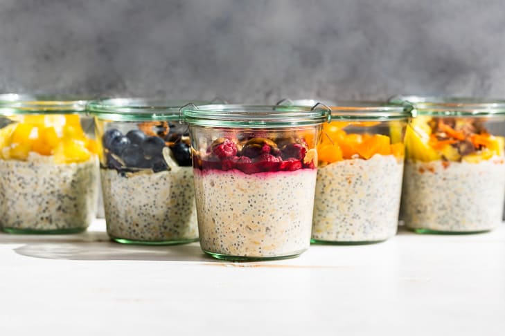 5 of the 10 Overnight Oats flavors on a white background and grey backdrop, (tropical, blueberry almond, PBJ, creamsicle, and carrot cake).
