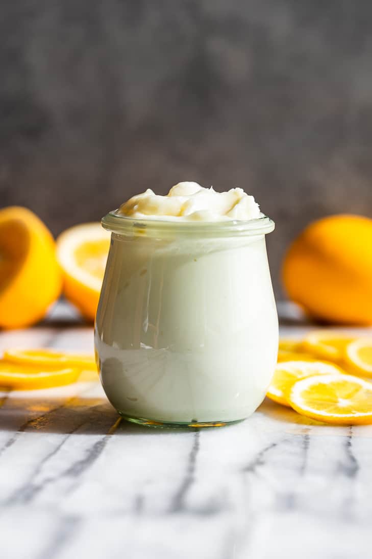 A jar of Lemon Cream Body Butter on a marble background with lemon slices around it.