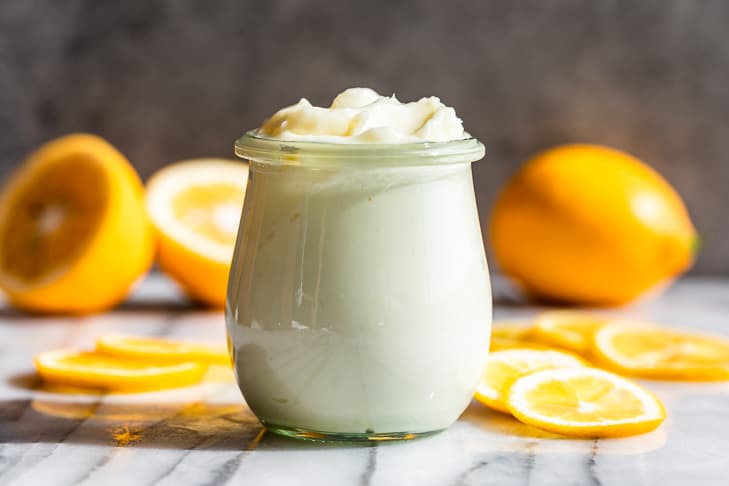 Lemon Cream Body Butter in a small jar on a marble surface with lemon slices around it.