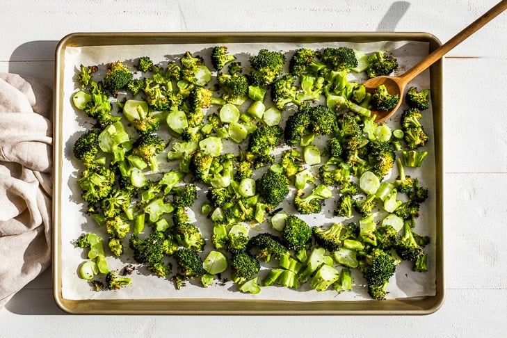 Broccoli florets being tossed together with garlic, olive oil and sea salt on a baking sheet.