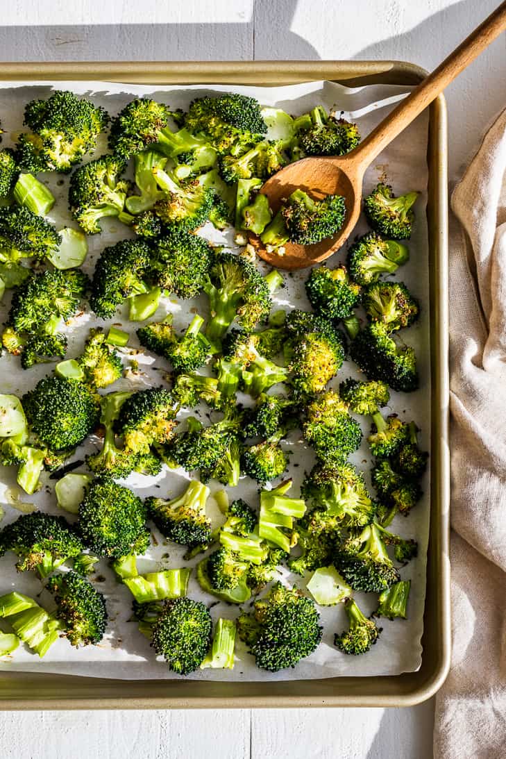 A gold sheet pan with Oven Roasted Broccoli with a wooden spoon.