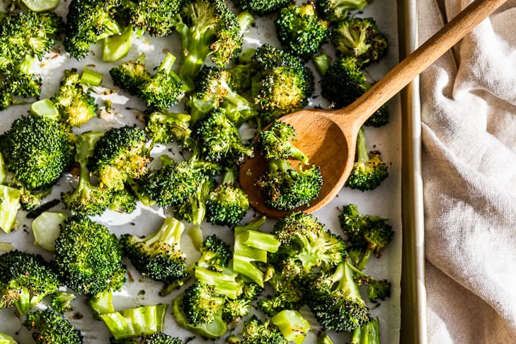 Sheet pan with Oven Roasted Broccoli and a wood spoon.
