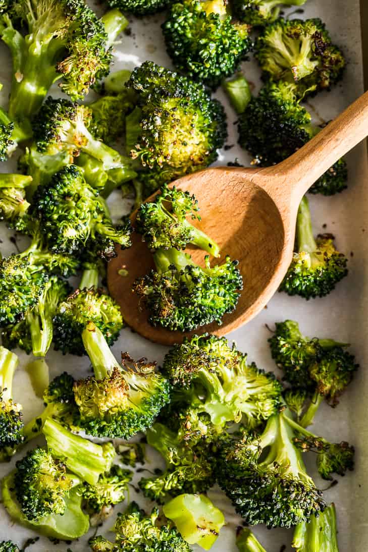 Oven Roasted Broccoli being scoop off the sheet pan with a wooden spoon.