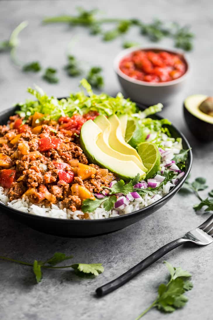 Slow Cooker Salsa Beef piled into a taco bowl with avocado, chopped onion, and letuce.