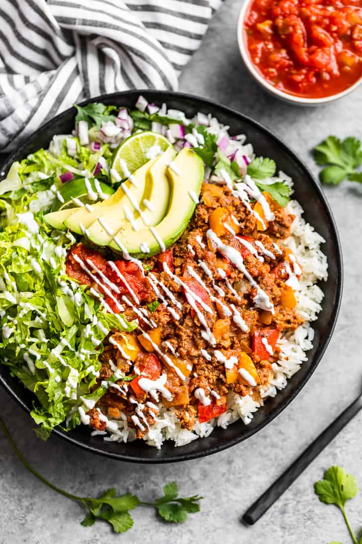 A bowl full of rice topped with Salsa Beef, lettuce, avocado, red onion, and salsa.