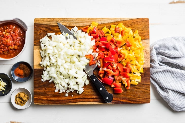 Chopped up onions and peppers on a wooden cutting board.