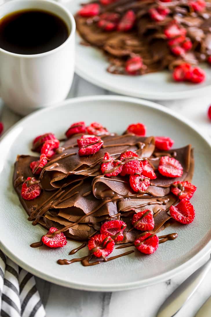 Double Chocolate Crepes topped with raspberries on a grey plate with a cup of coffee.