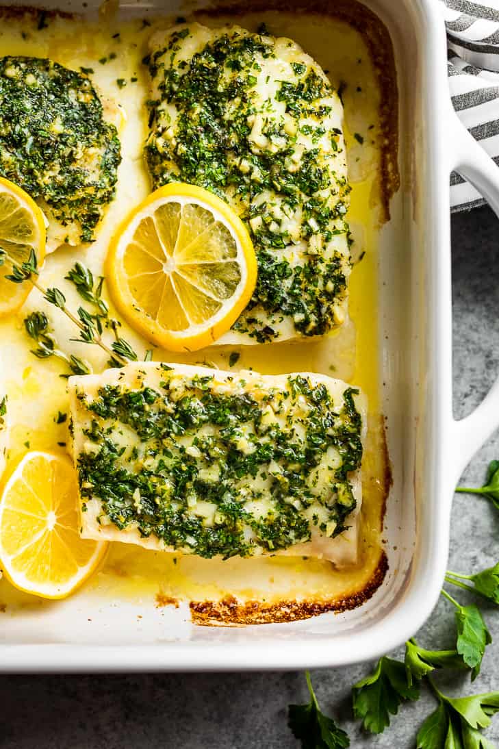 A straight down close view of the lemon herb baked cod in a white baking dish with parsley springs.