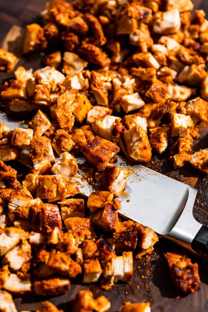 The chipotle chicken being chopped up on a wooden cutting board.