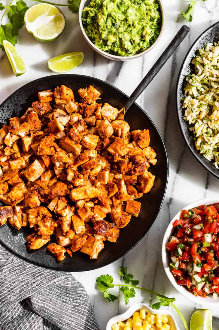 Copycat Chipotle Chicken on a black plate with toppings of guacamole, pico de gallo, corn and rice around it.