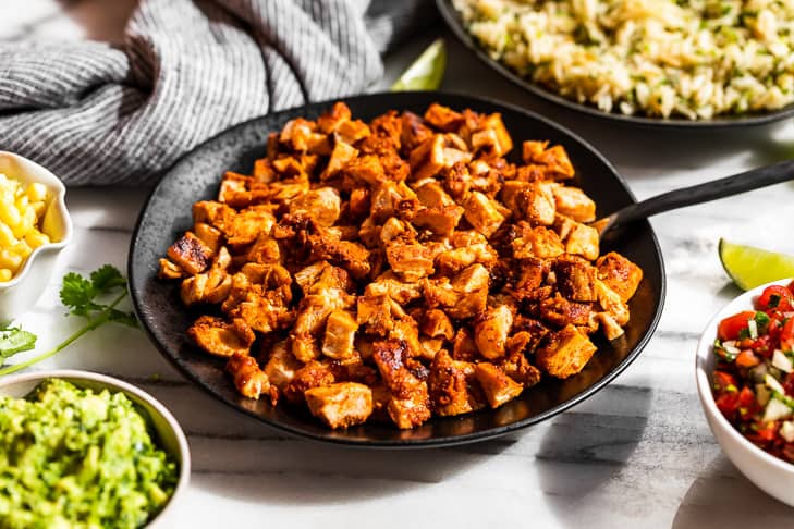 A bowl of Copycat Chipotle Chicken with the burrito bowl toppings around it.