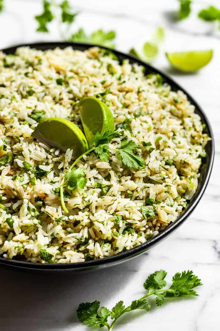 A black bowl filled with Cilantro Lime Rice with lime wedges and cilantro on top.