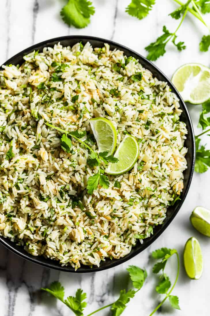Straight down view of cilantro lime rice in a black bowl with lime wedges and cilantro around it.