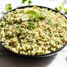 A black bowl filled with Cilantro Lime Rice with lime wedges and cilantro around it.