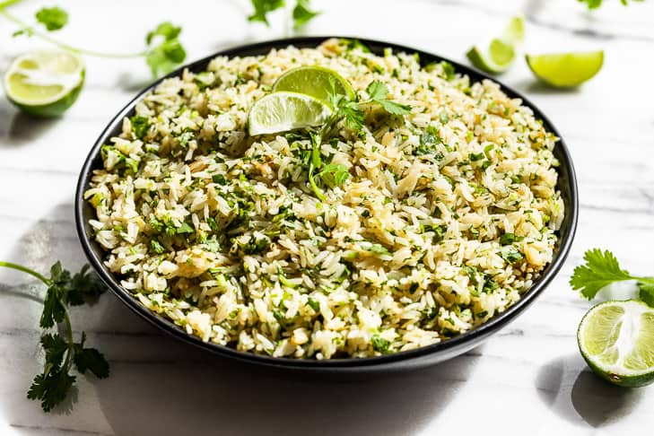 A black bowl filled with Cilantro Lime Rice with lime wedges and cilantro around it.