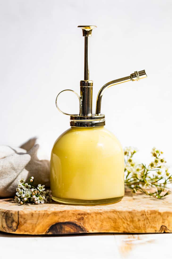 Lotion in a glass bottle with a gold pump handle on a wooden board with small white flowers in the background.