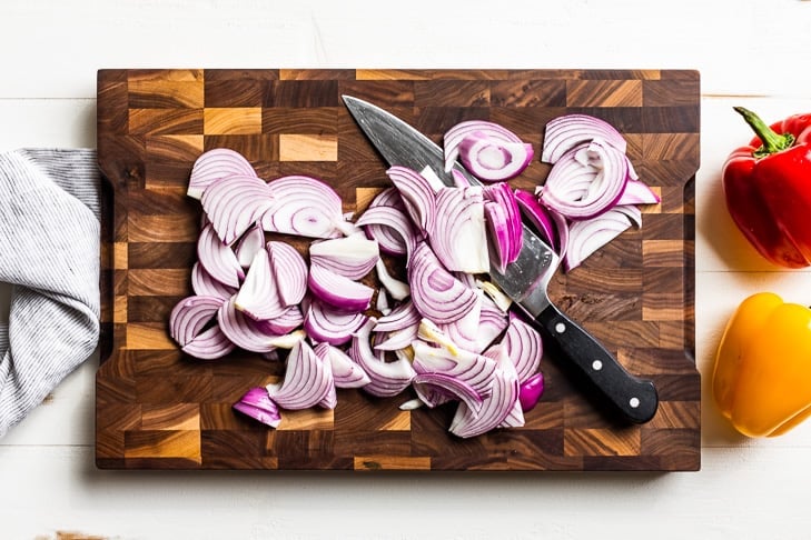 The onions for the fajita veggies cut up into half moon slices on a wooden cutting board.