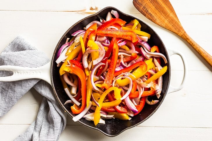 Sautéing the fajita veggies in a large white skillet.