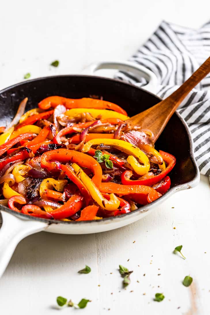 A side view of a white skillet filled with Fajita Veggies being scooped out with a wooden spoon.