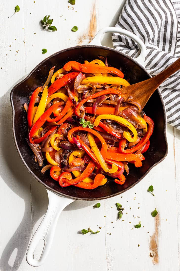 Straight down view of a white skillet with Fajita Veggies and oregano around it.