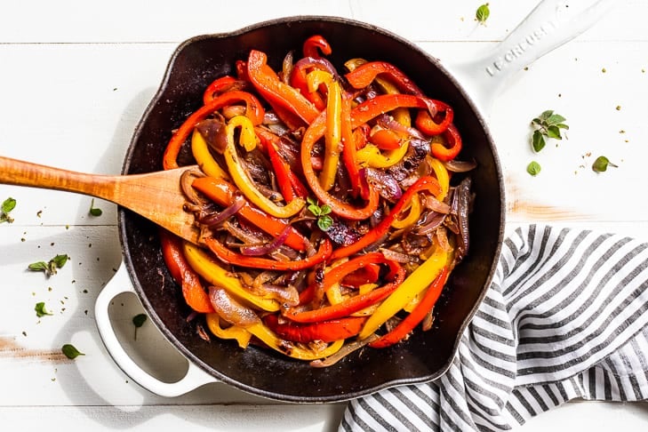 The finished Fajita Veggies in a white skillet with a wooden spoon.