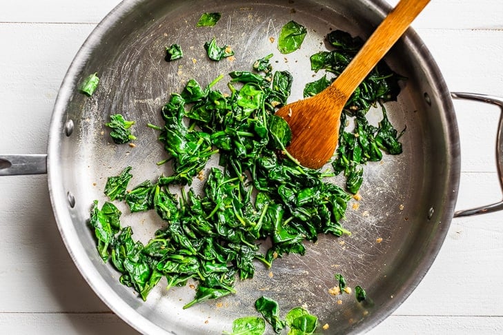 The barely wilted spinach sautéed in a stainless steel skillet with a wooden spoon.