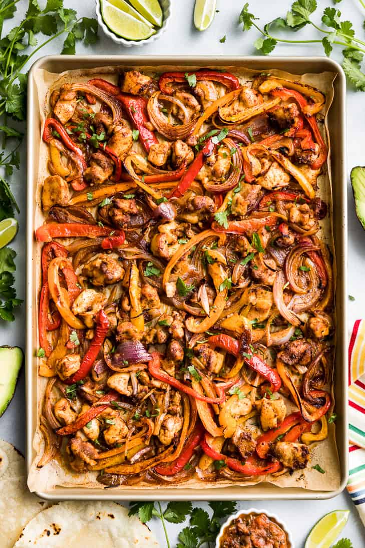 Healthy Chicken Sheet Pan Fajitas with lime wedges and cilantro around it.