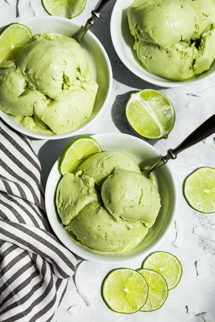 Three bowls of Coconut Lime Ice Cream with lime slices and a striped linen.