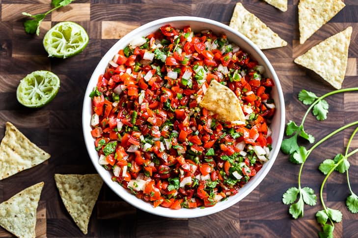 Pico de gallo in a white bowl on a wooden cutting board.