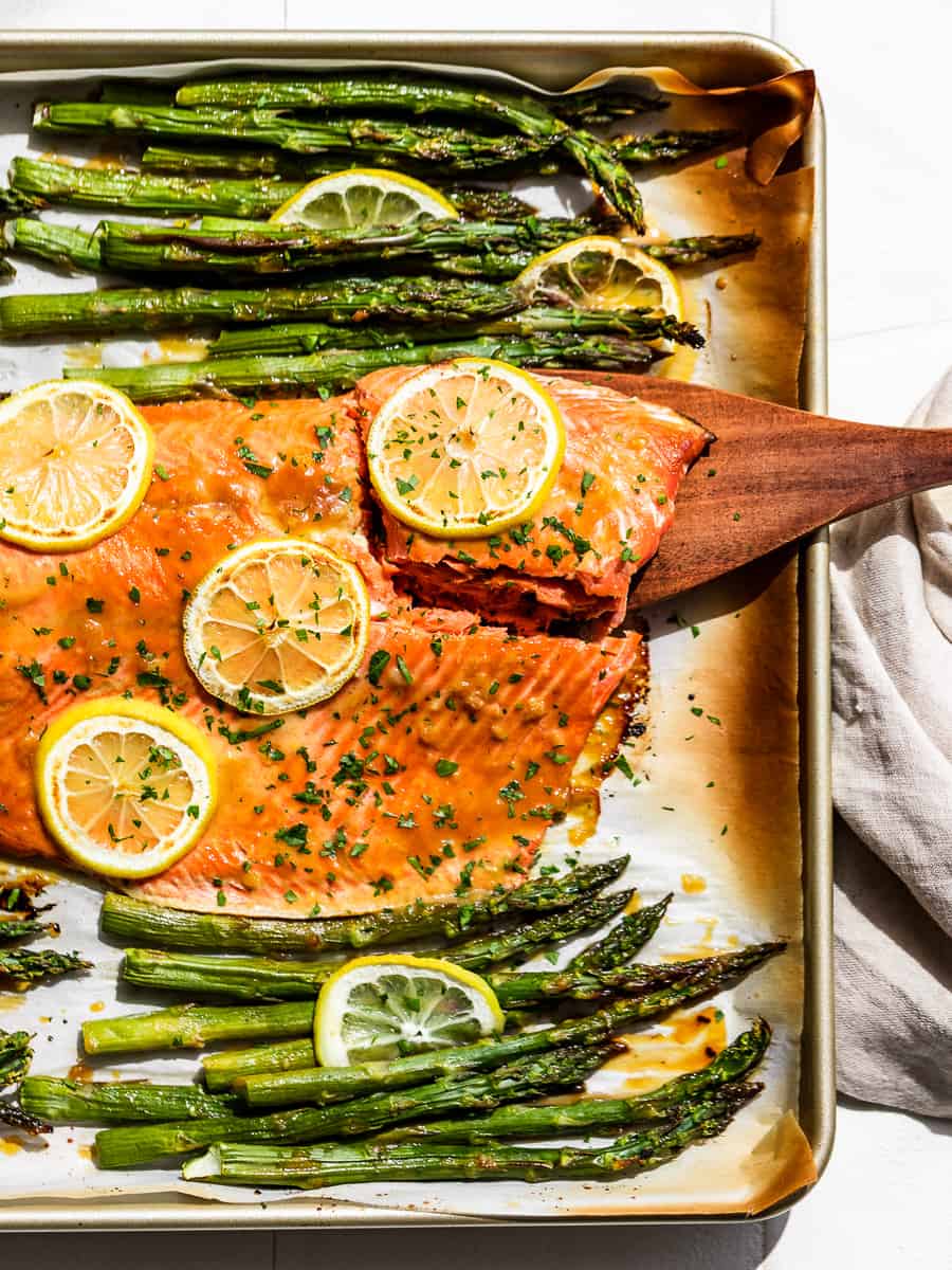 A straight down view of Honey Dijon Salmon and Asparagus with a piece of salmon being lifted out.