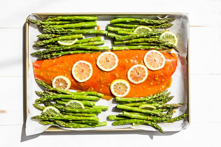 The salmon and asparagus on a sheet pan with the glaze and lemon slices.