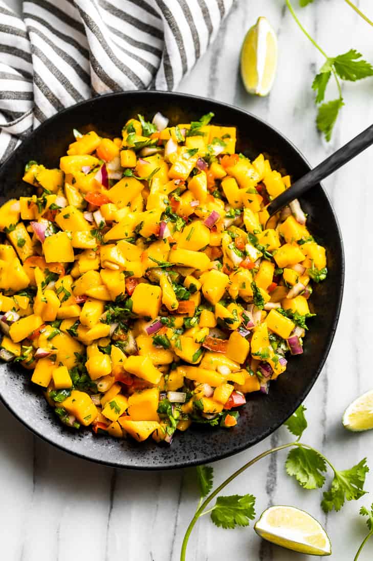Mango Salsa in a black bowl with cilantro and lime wedges around it.