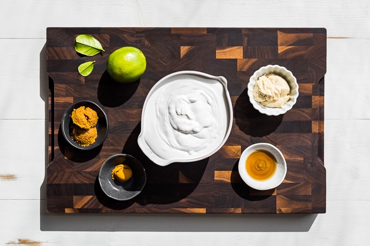 The coconut milk, curry paste, turmeric, fish sauce, and cashew butter measured out on a wooden cutting board.